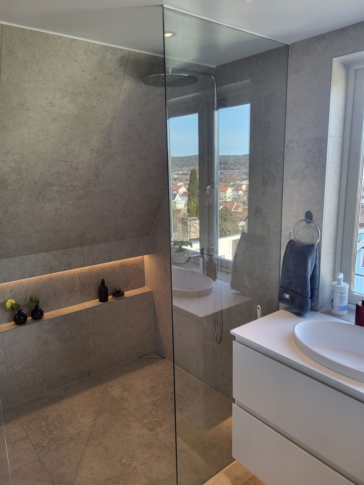 Renoverat badrum: Ljus beige sten, fristående badkar, glasdusch, takfönster